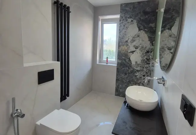 Nowoczesna łazienka premium z prysznicem typu walk-in, dekoracyjną ścianą z kamienia, nablatową umywalką i czarnymi akcentami – realizacja wykończenia wnętrz DECO MAX.
